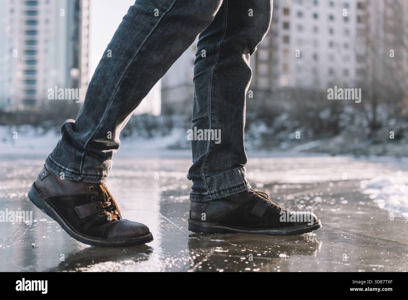 Stiefel stehen auf vereistem Boden, die die Rutschgefahr auf einem gefrorenen, rutschigen Wintergrund veranschaulichen. Ein Mann läuft vorsichtig auf einer vereisten Straße weiter Stockfoto