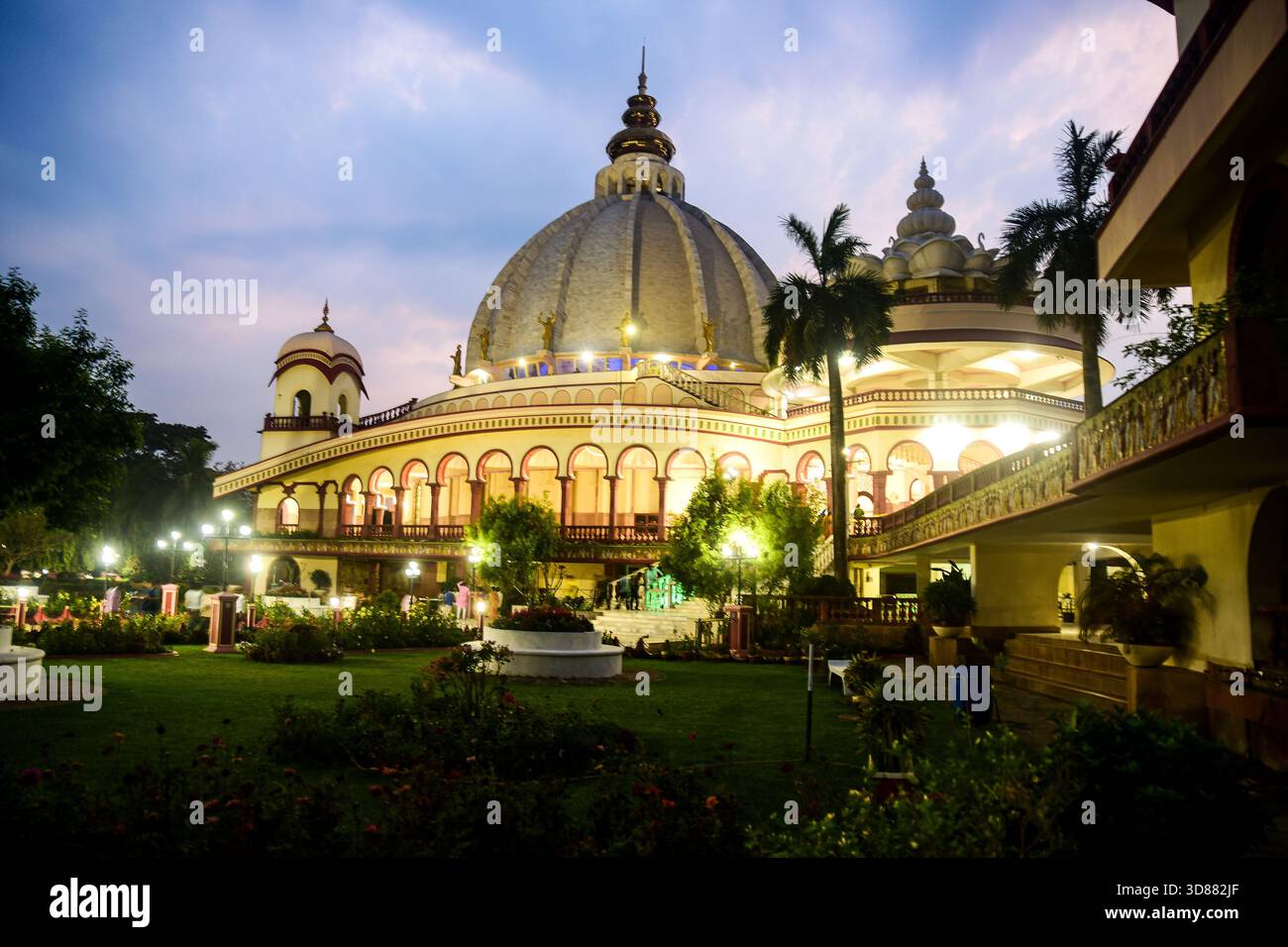 ISKON-Tempelkomplex bei Dämmerung mit Kuppel, Bögen und beleuchtetem Garten Stockfoto