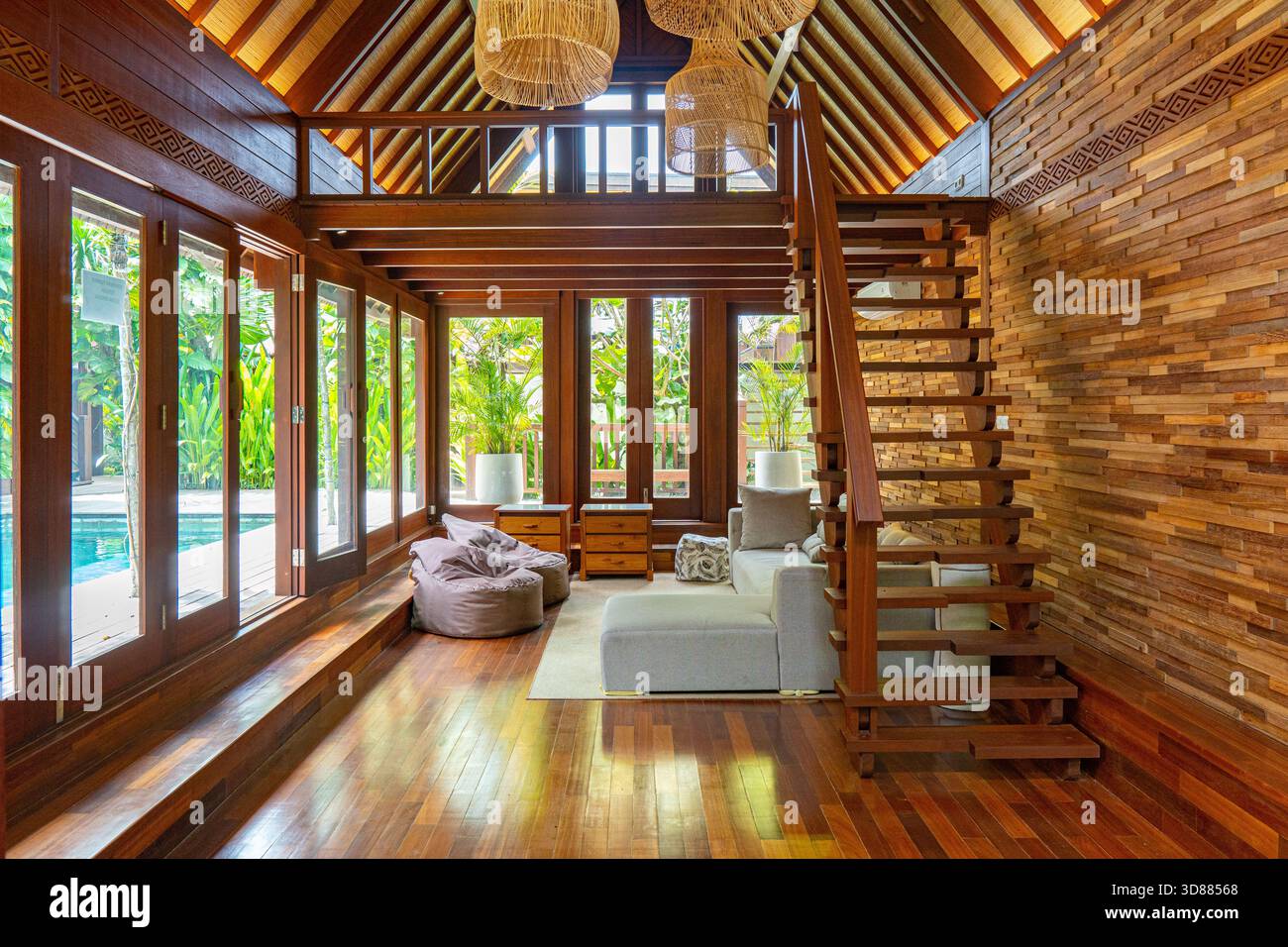 Ein großes offenes Wohnzimmer mit einer Holztreppe, die zu einem Loft führt. Der Raum verfügt über Tageslicht und eine gemütliche, einladende Atmosphäre. Weiter Stockfoto