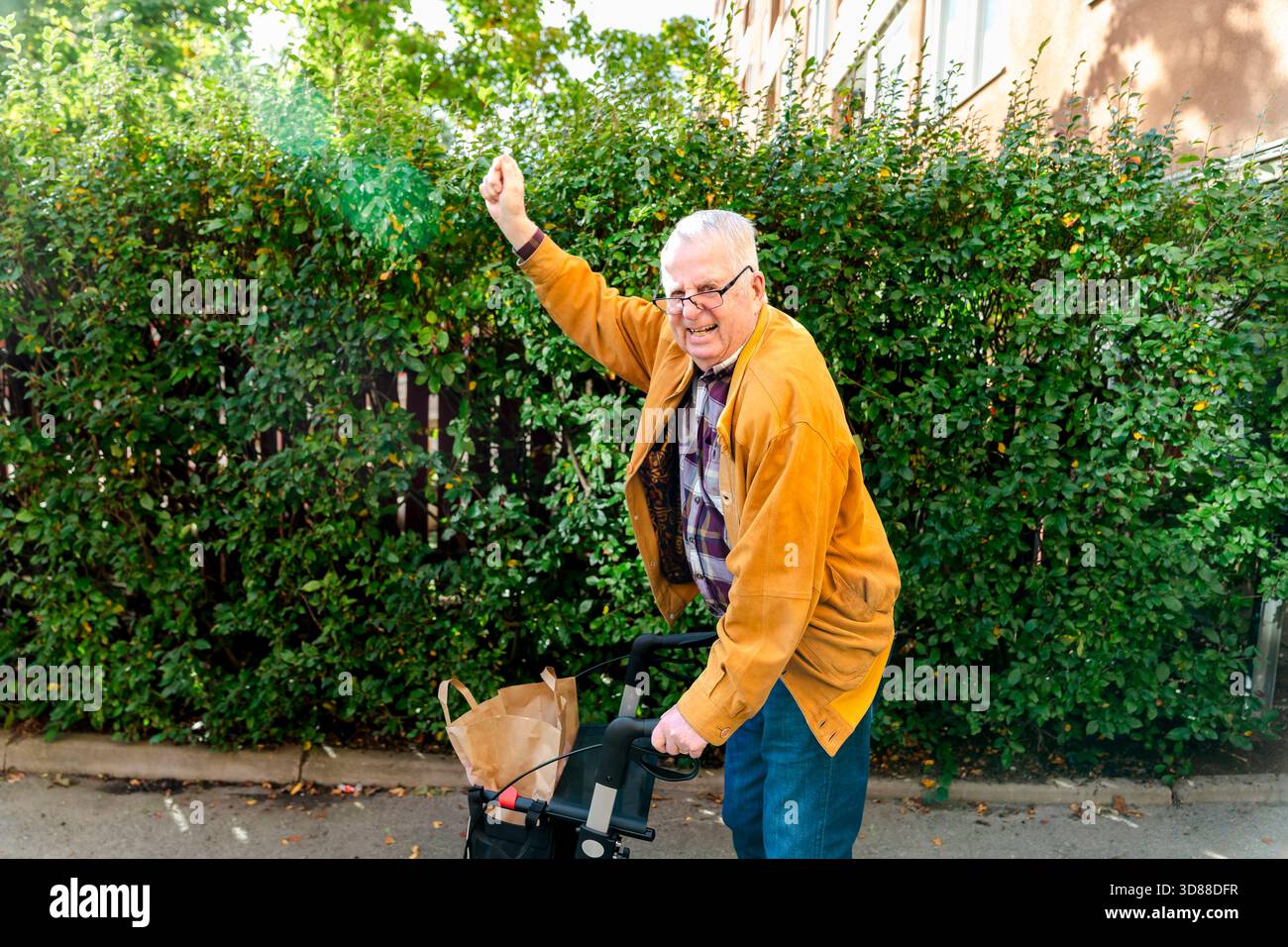 Porträt eines fröhlichen älteren Mannes, der mit Rollator vor Pflanzen steht Stockfoto