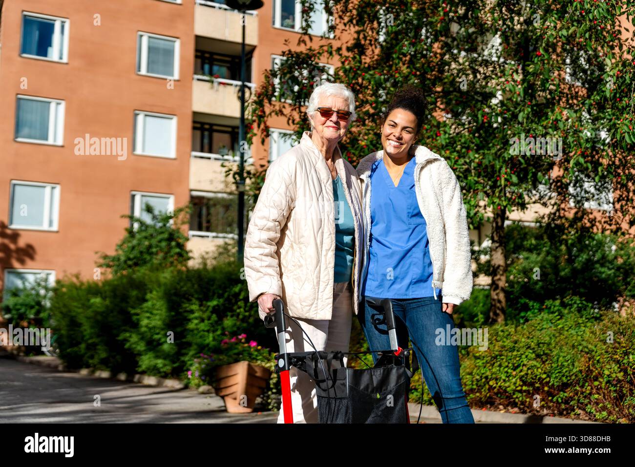 Porträt einer lächelnden Krankenschwester, die bei sonnigem Tag mit älterer Frau im Park steht Stockfoto