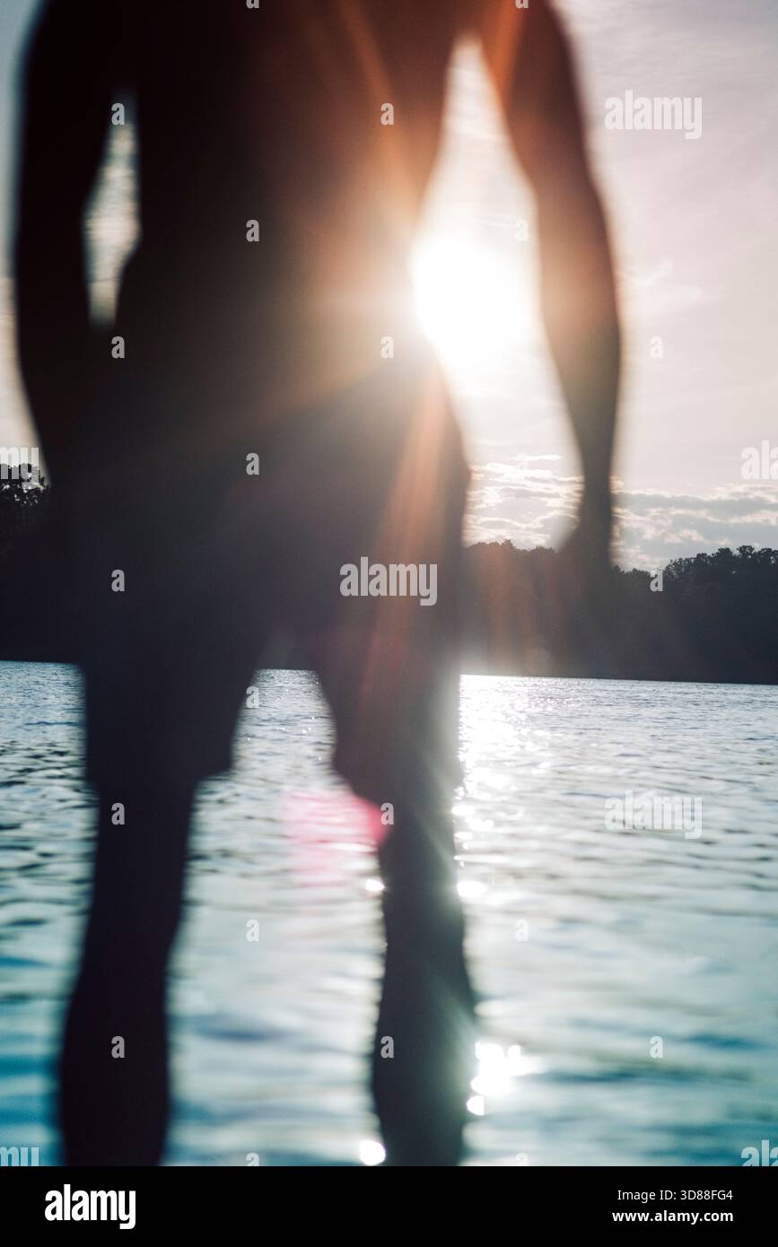 Sonnenlicht leuchtet hell, während der Mann in der Nähe des Sees steht Stockfoto
