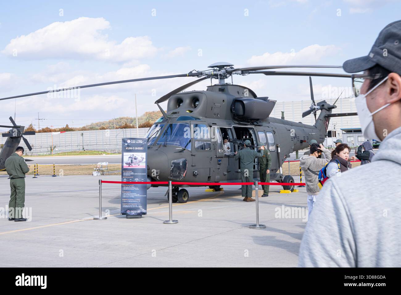 Ein militärischer Hilfshubschrauber, der auf einem Flugplatz geparkt ist und von einem Besatzungsmitglied gewartet wird, zeigt sein detailliertes Rotorsystem, das Cockpit-Design, A Stockfoto