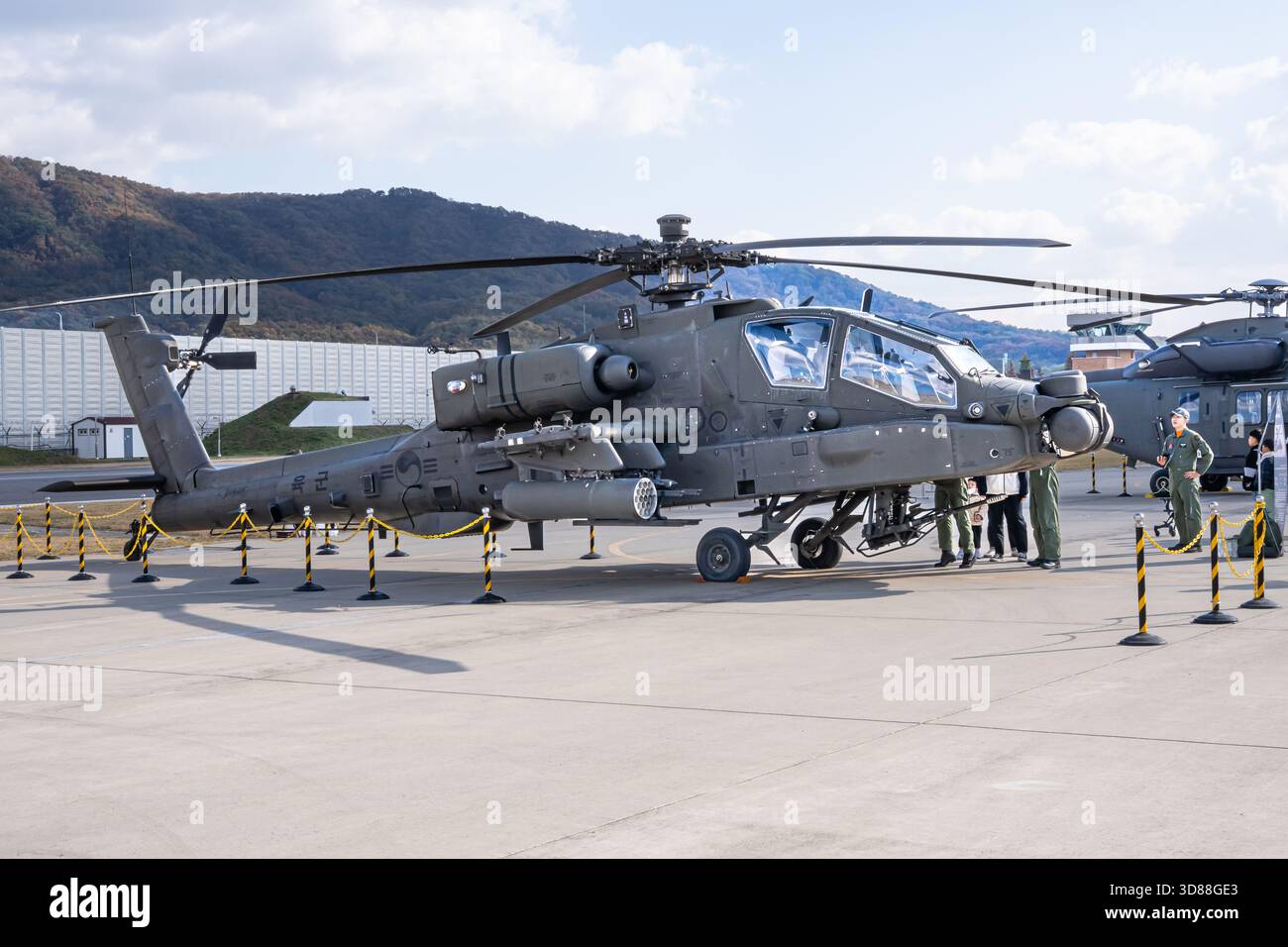Ein militärischer Hilfshubschrauber, der auf einem Flugplatz geparkt ist und von einem Besatzungsmitglied gewartet wird, zeigt sein detailliertes Rotorsystem, das Cockpit-Design, A Stockfoto