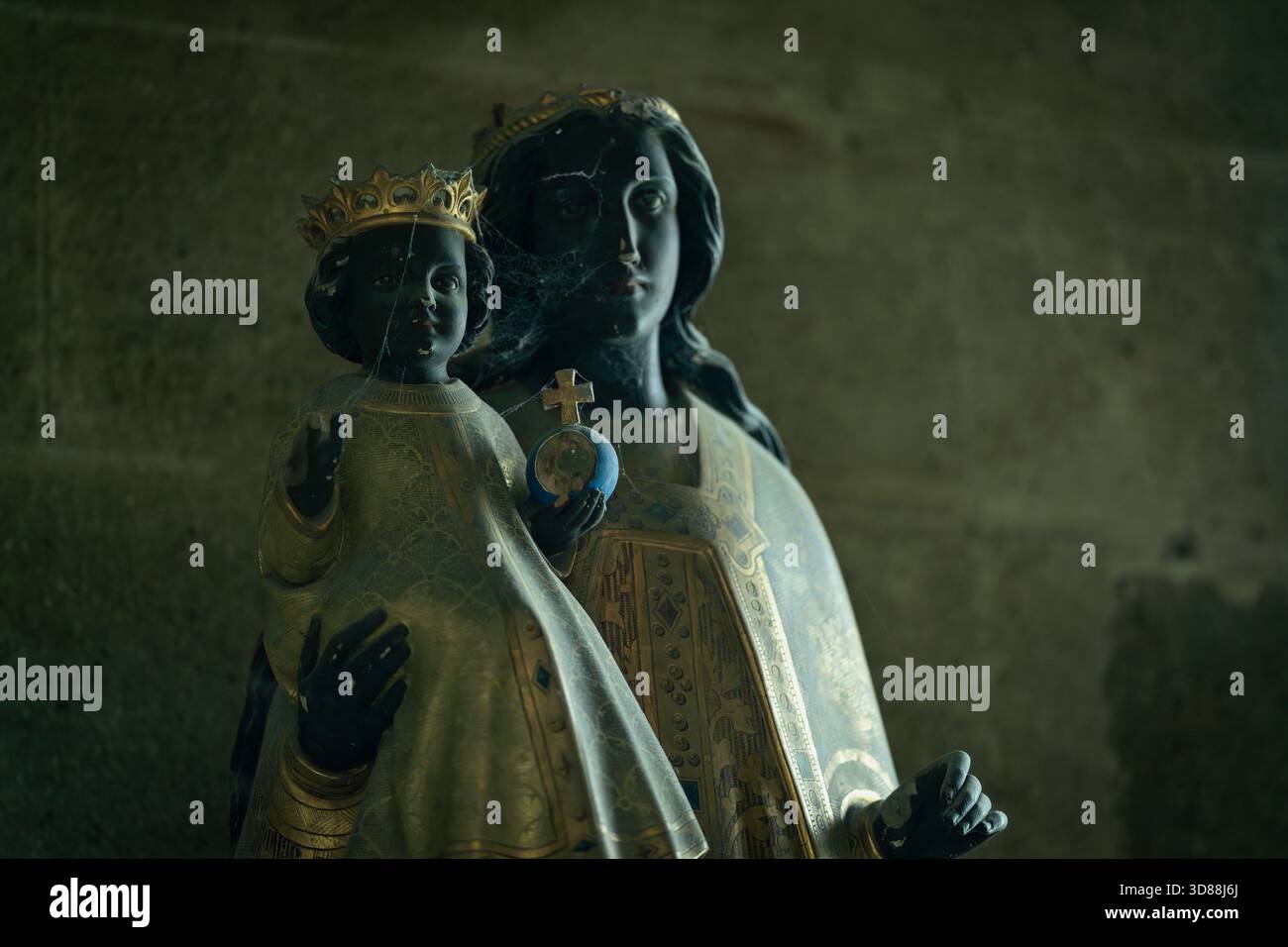 Antike Statue der Jungfrau Maria und des Jesuskindes im Mont Saint-Michel. Verwitterte Madonna-Kind-Skulptur mit goldenen Details im dunklen Inneren. Stockfoto