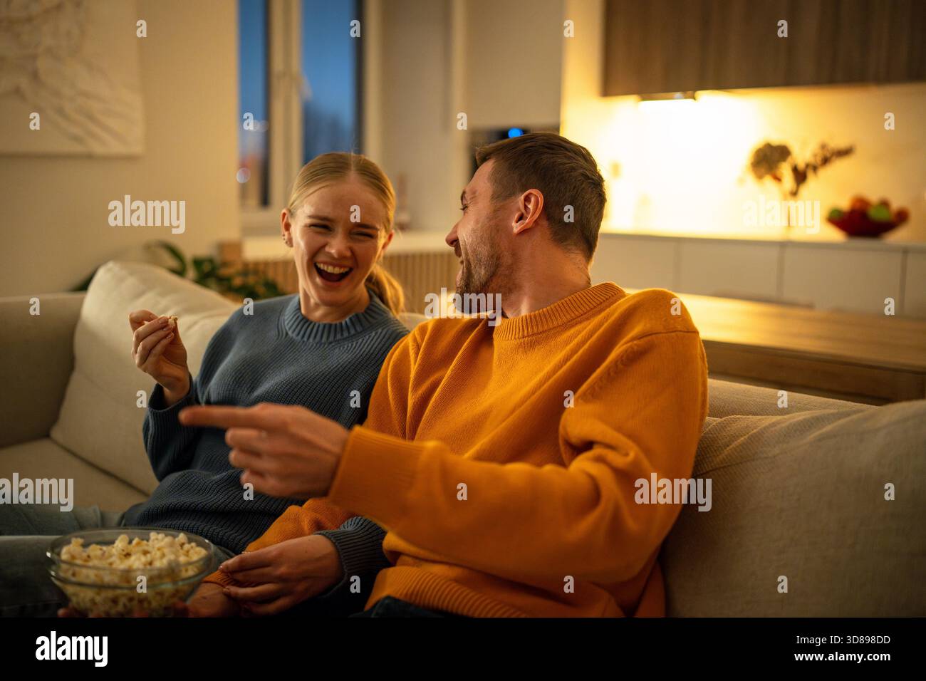 Ein Paar lacht zu Tränen, während es Filme ansieht und macht am Freitagabend zu Hause Witze auf dem Sofa. Mann und Frau rollten sich auf der Couch mit Tränen und breitem Lächeln, während der Filmnacht tauschten || Model wurde veröffentlicht Stockfoto