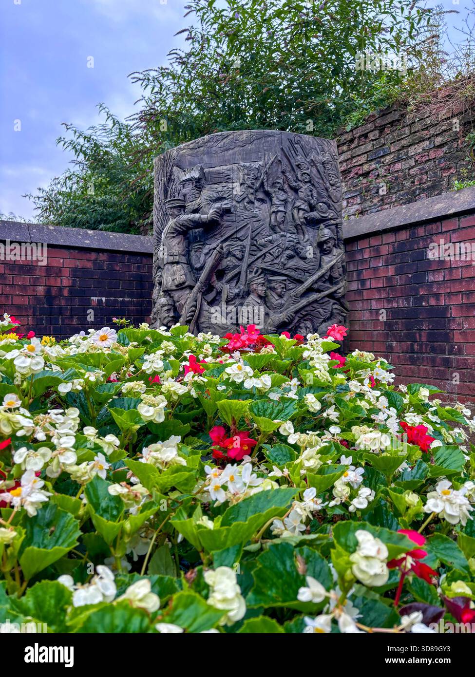 Steinskulpturales Relief war Memorial umgeben von weißen und roten Begonia Blumen und roten Ziegelmauern Stockfoto