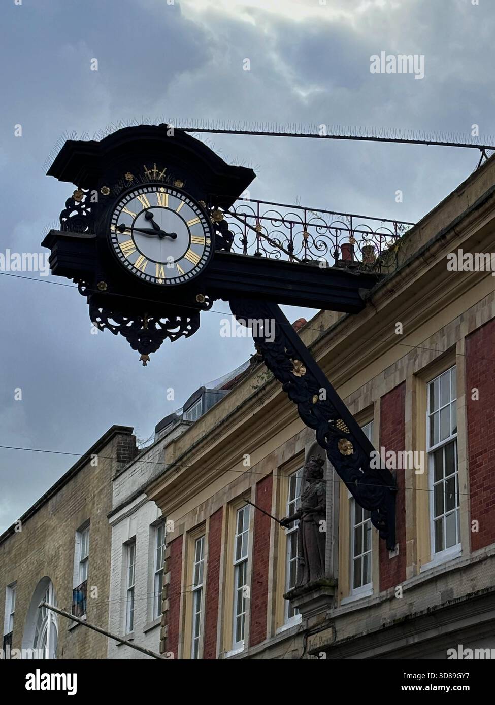 Die öffentliche Uhr in Schwarz und Gold in einem historischen Gebäude aus roten Ziegeln in einer City Street in Winchester, Großbritannien Stockfoto