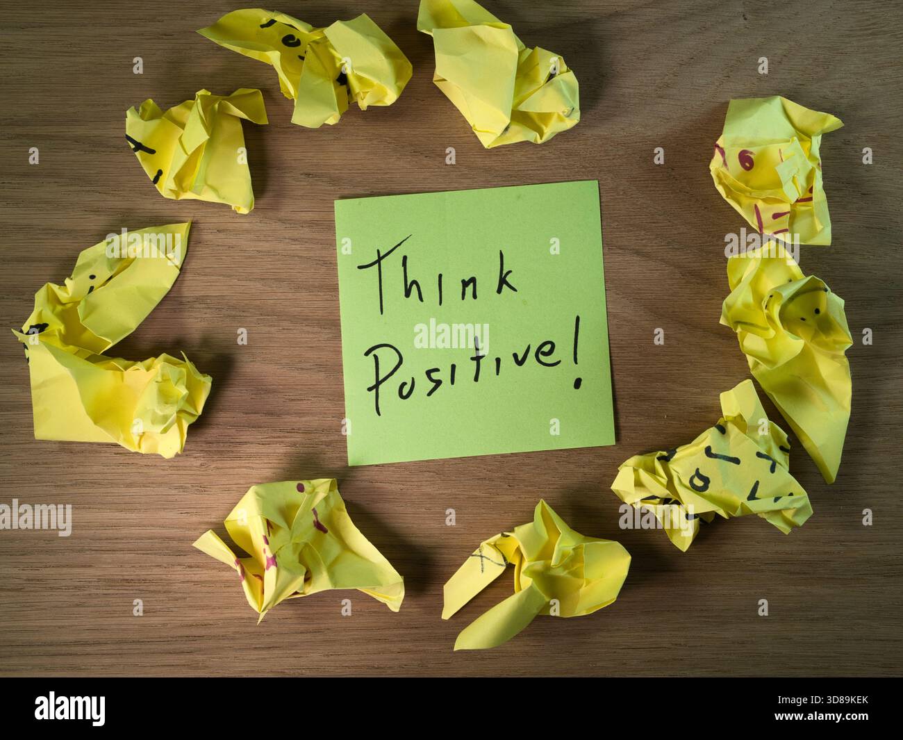 Denken Sie Positiv! Grüne Notiz und zerknittertes Papier – Grüne Haftnotiz mit „positiv denken!“ Nachricht umgeben von zerknitterten gelben Papieren auf einem Holztisch. Stockfoto
