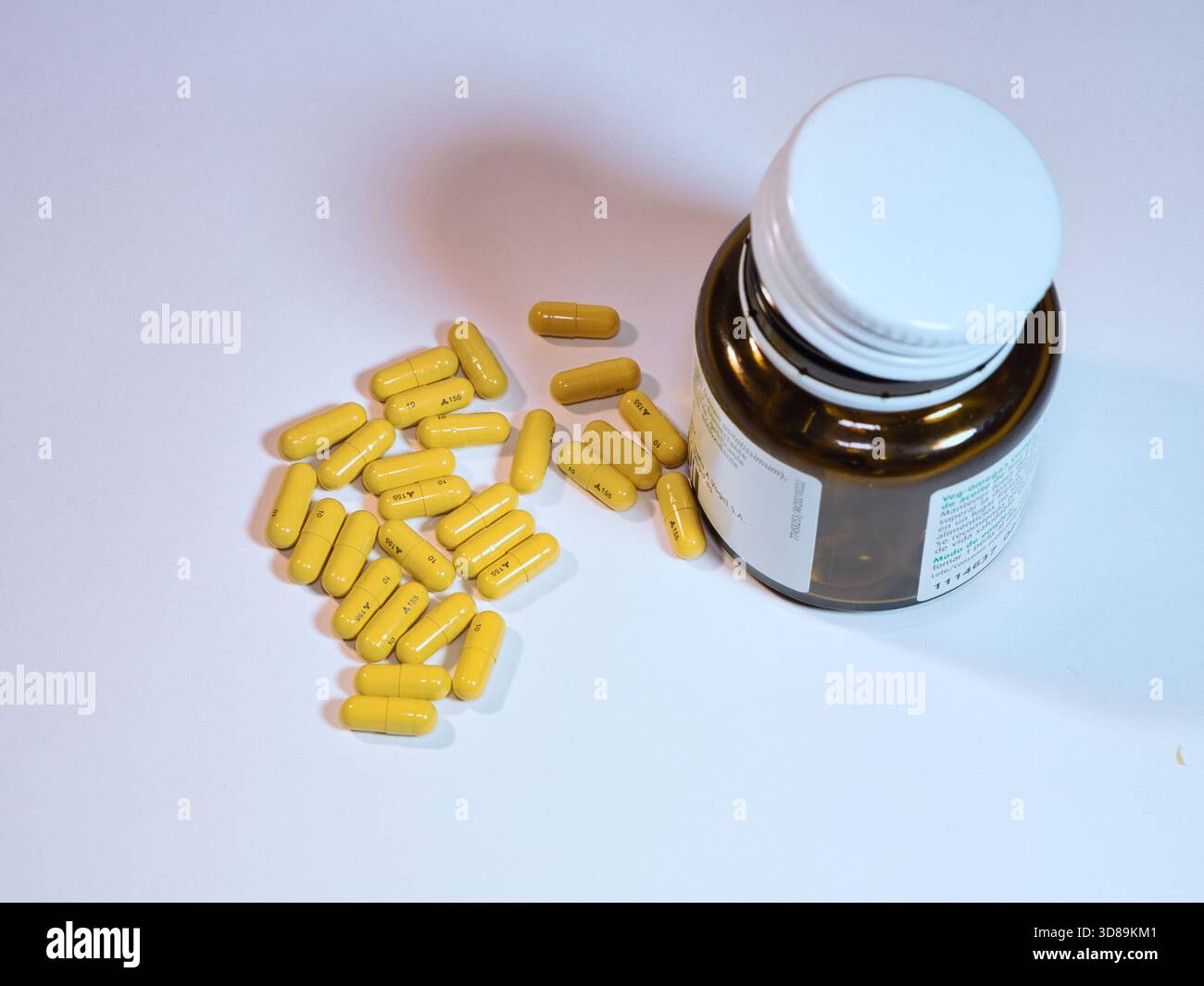 Gelbe Kapseln und Arzneimittelflasche - Nahaufnahme gelber Kapseln, die aus einer braunen Arzneimittelflasche auf einer sauberen weißen Oberfläche verschüttet wurden. Ideal für das Gesundheitswesen, Stockfoto