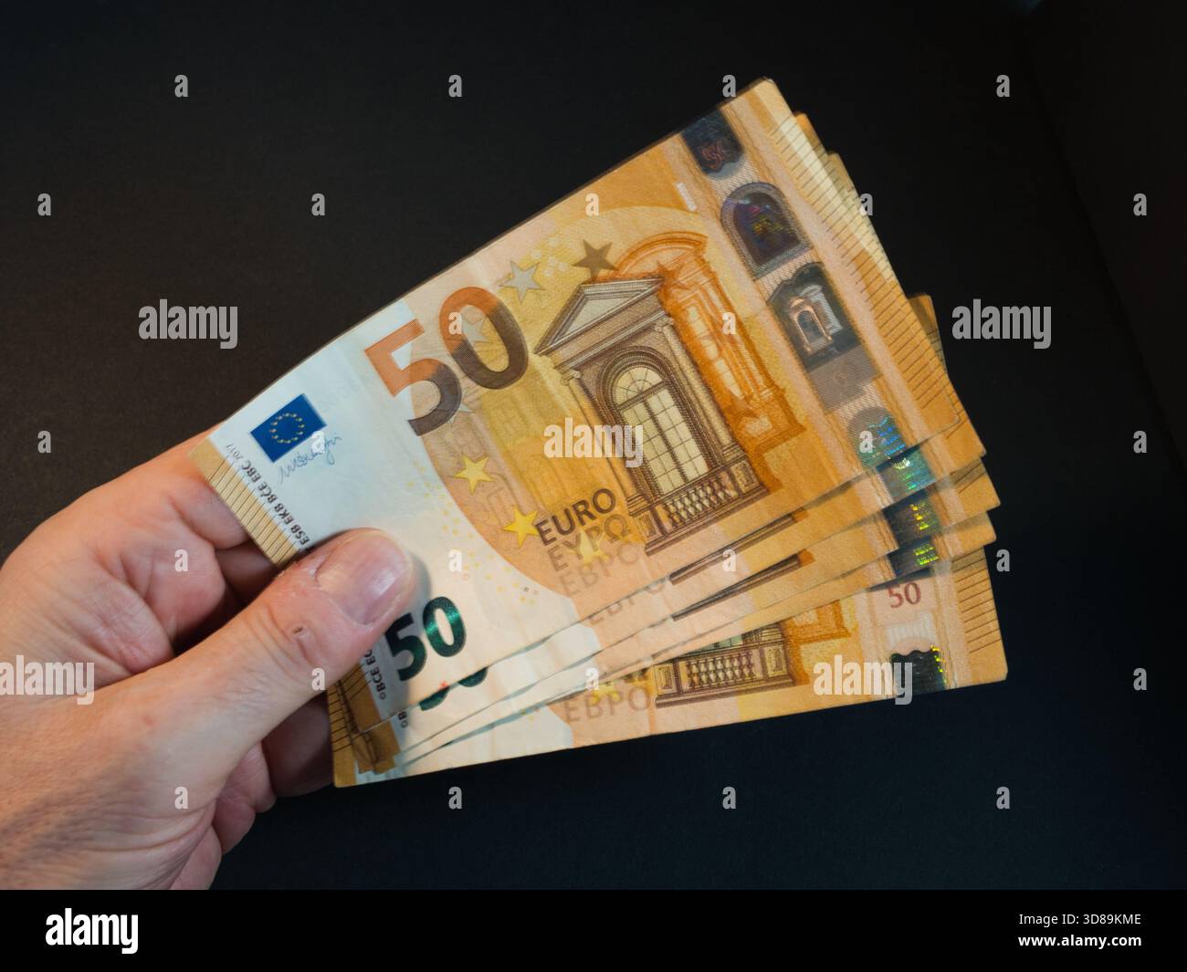 Hand mit fünfzig Euro-Banknoten - Nahaufnahme einer Hand, die mehrere 50-Euro-Banknoten vor dunklem Hintergrund hält und auffächert. Symbolisiert Finanzen Stockfoto