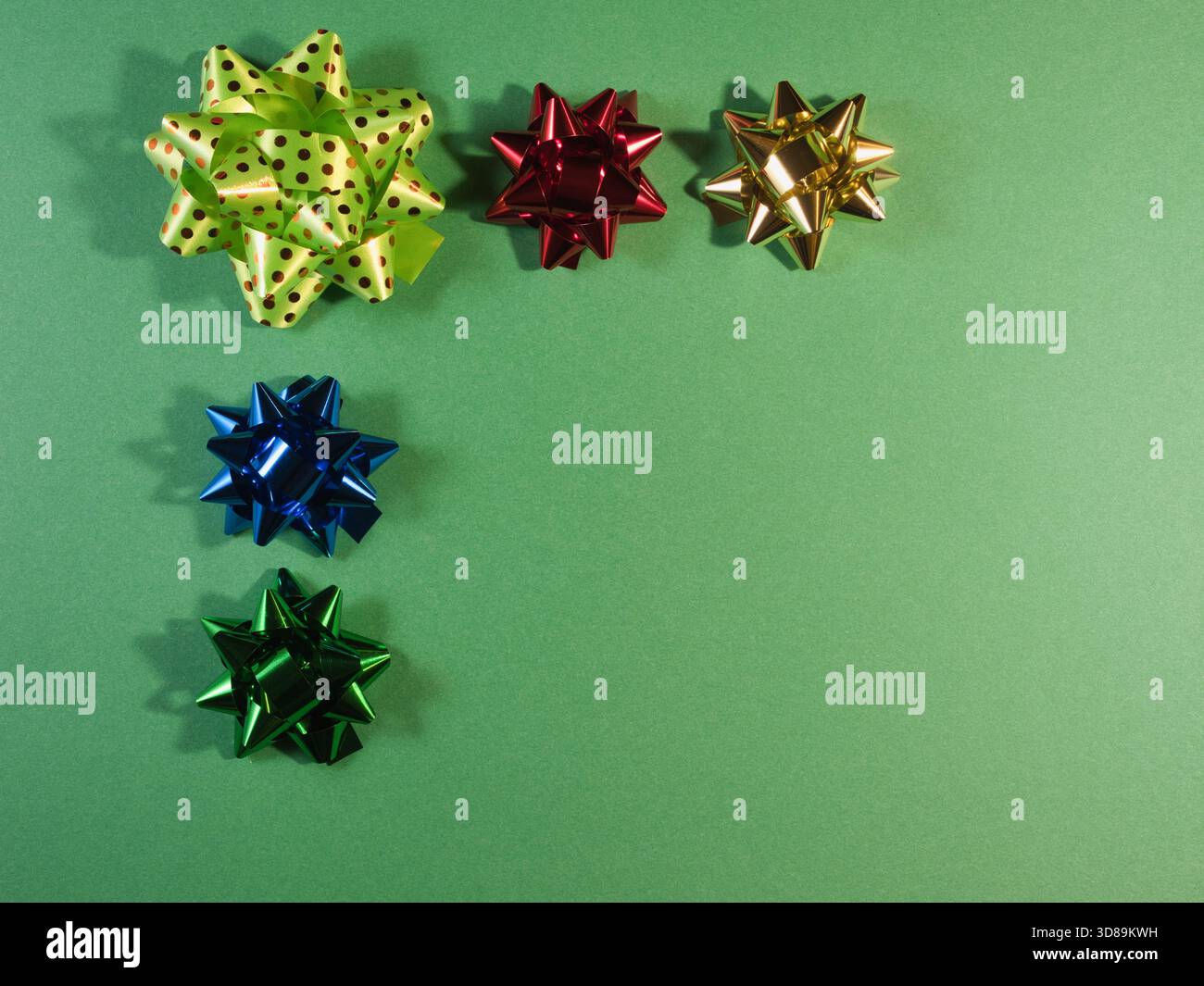 Bunte Geschenkschleifen auf grünem Hintergrund - fünf leuchtende, metallische Geschenkschleifen in verschiedenen Farben und Designs, einschließlich Polka Dots, auf einem strukturierten grünen Pops Stockfoto