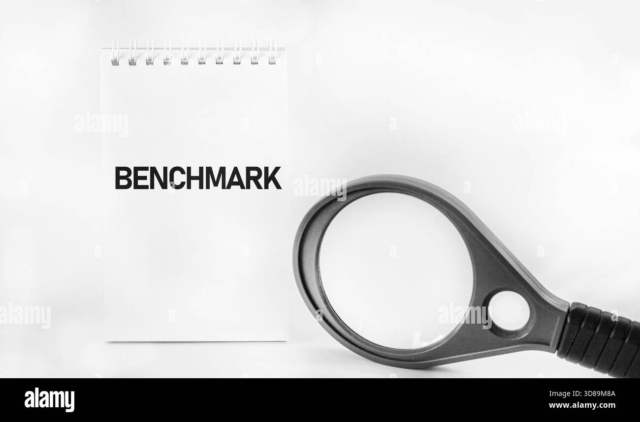 Das Benchmark-Geschäftskonzept. Das Wort BENCHMARK steht auf einem weißen Stück Papier neben einer Lupe Stockfoto