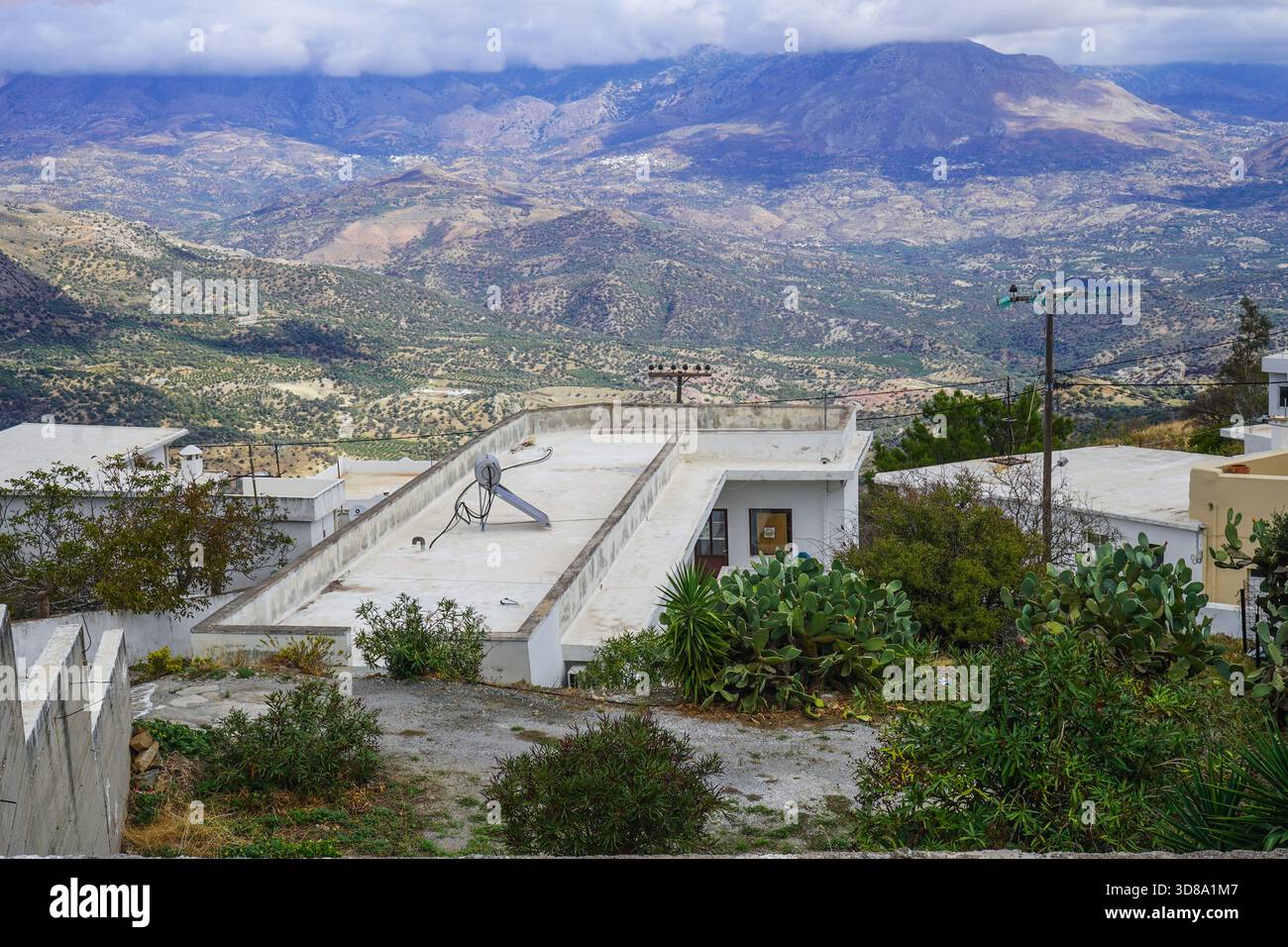 Blick von einer Dorfstraße in Melampes, Kreta, mit Blick auf ein niedriges Dach mit Solarheizung und TV-Antenne in Richtung des dramatischen Himmels. Stockfoto