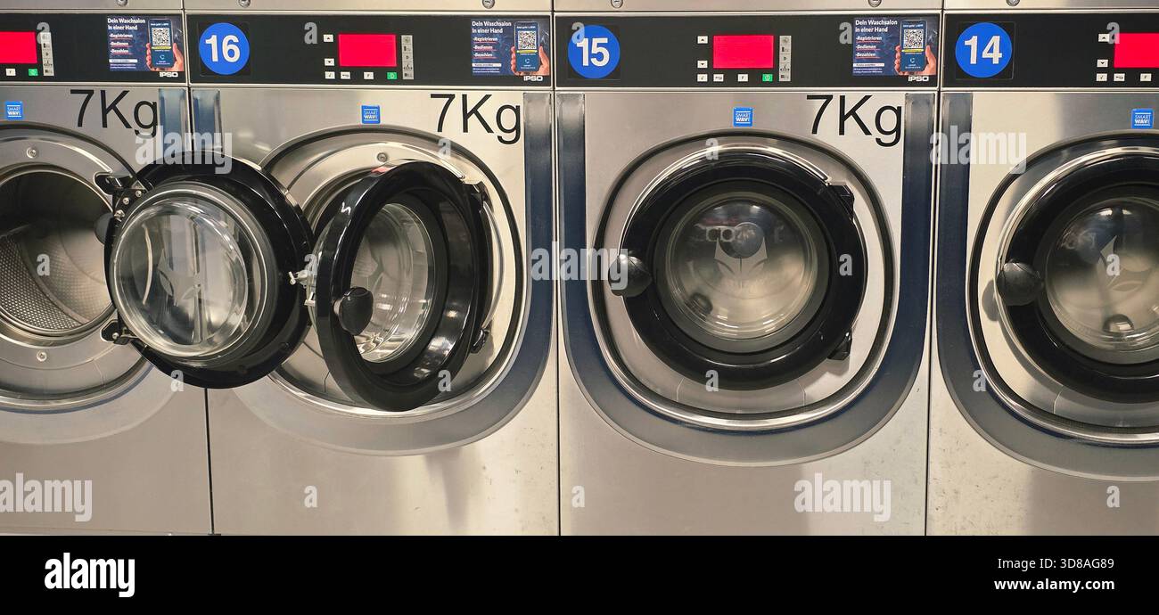 Berlin, Deutschland - 25. September 2025: Gewerbliche Waschmaschinen im Waschsalon mit offener Tür und digitaler Steuerung. Stockfoto