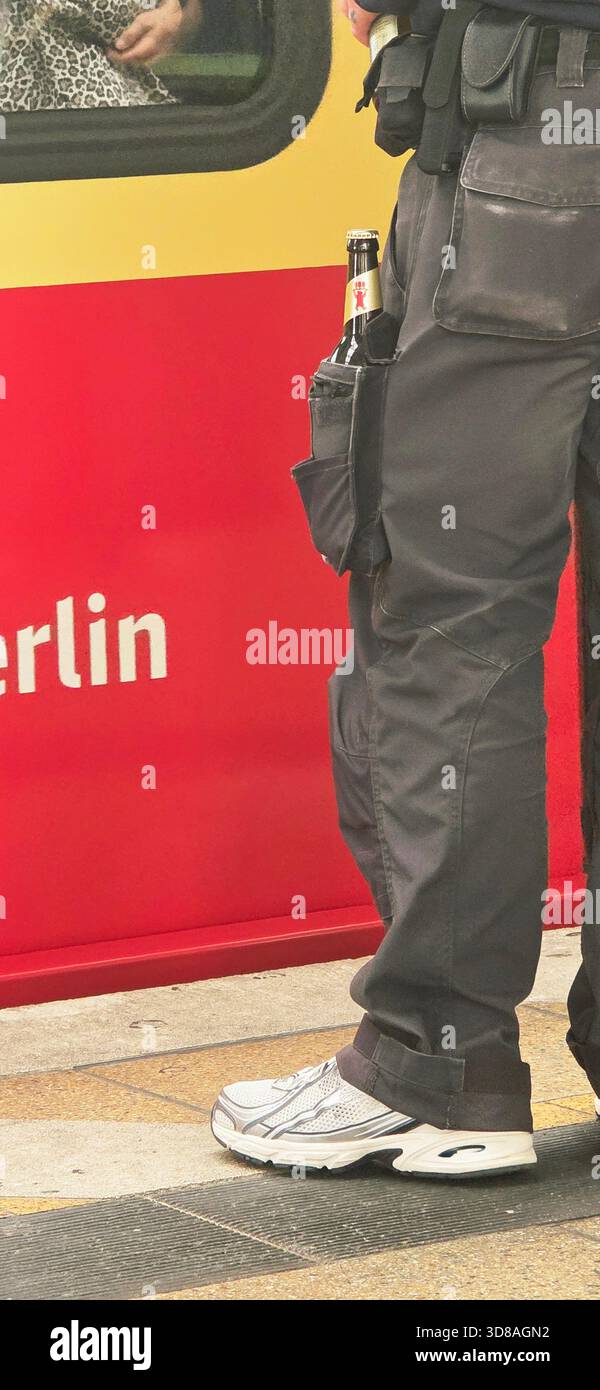 Berlin, Deutschland - 17. September 2025: . Der Polizist steht neben dem Zug mit einem Getränk in der Tasche in Berlin - Smartphone-aufgenommenes Stockfoto