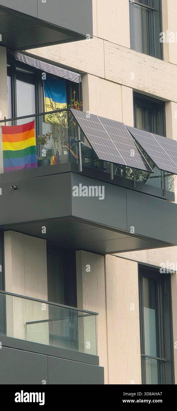 Berlin, Deutschland - 25. September 2025: Moderner Balkon mit Solarpaneelen und einer leuchtenden Regenbogenfahne, die in der Brise winkt. Stockfoto