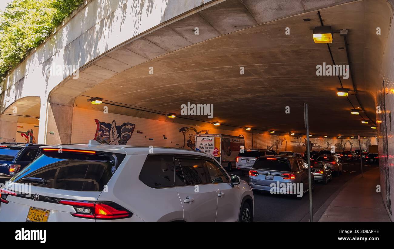 Washington D.C., USA, 25. Mai 2025. Die Autos fahren langsam durch einen schwach beleuchteten Tunnel, der mit gefliesten Wandgemälden geschmückt ist, während sich der Verkehr aufbaut. Stockfoto
