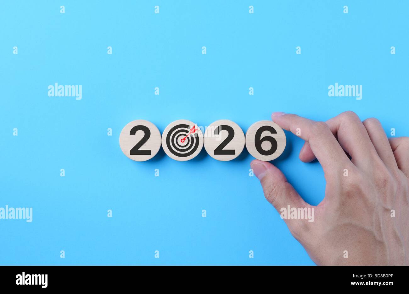 2026 Konzept der Zielsetzung. Händige Anordnung von Holzblöcken und Zielsymbol auf blauem Hintergrund, symbolisiert Geschäftsplanung, Vision-Ausführung, Zukunft Stockfoto