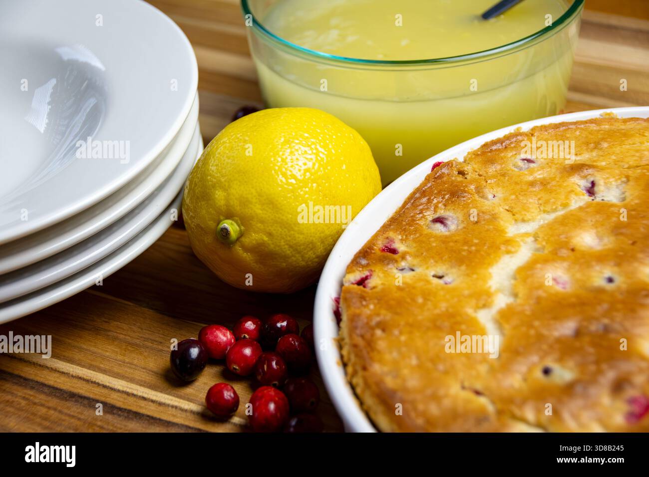 Der klassische Geschmack von Zitrone und Preiselbeere, perfekt für einen traditionellen Urlaub. Die ganze Schüssel mit Zitrone und Glasur neben dem hausgemachten Preiselbeerkuchen. Stockfoto