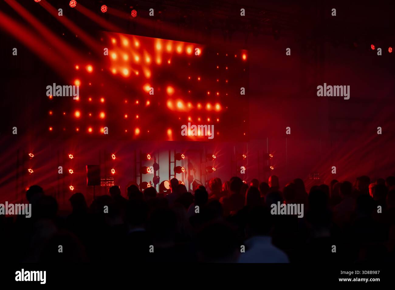 Die Menge versammelte sich vor einer Bühne, die von intensivem rotem Licht und LED-Wandeffekten beleuchtet wurde und eine dramatische Atmosphäre während einer großen Veranstaltung in der Halle schaffte Stockfoto