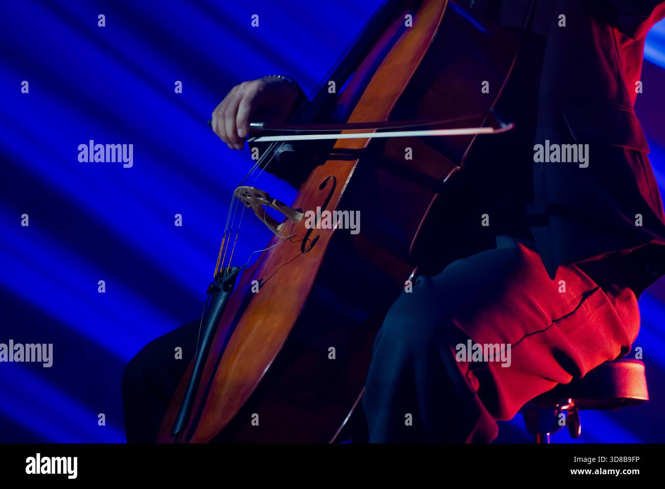 Live-Konzertszene, die eine detaillierte Ansicht eines Cellos und eines Bugs in Bewegung zeigt, während ein Darsteller unter dynamischer farbiger Beleuchtung spielt und ein lebendiges Musical A erzeugt Stockfoto