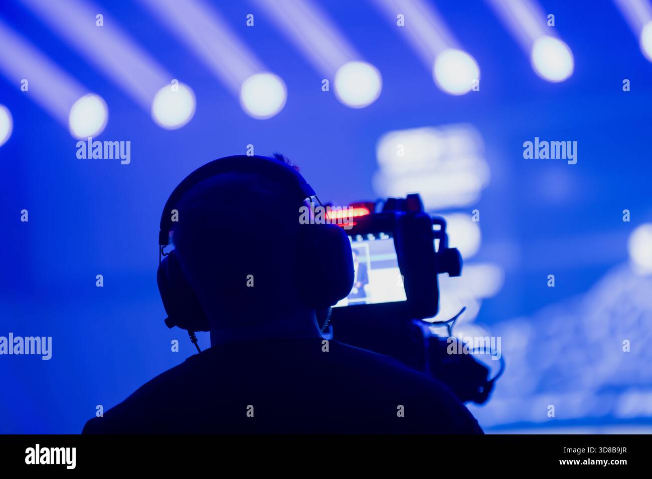 Kamerabediener filmt ein Live-Event unter intensiver blauer Bühnenbeleuchtung mit hellen Lichtkegeln und zeigt professionelle Broadcast- und Event-Produkte Stockfoto