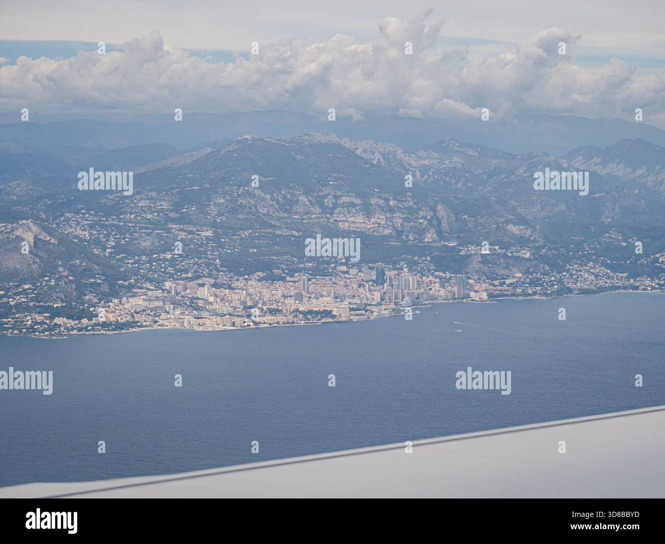Von einem Flugzeugfenster aus gesehen bietet sich ein Blick auf die urbane Küste Monacos, eingebettet zwischen dem Mittelmeer und der zerklüfteten Berglandschaft. Stockfoto