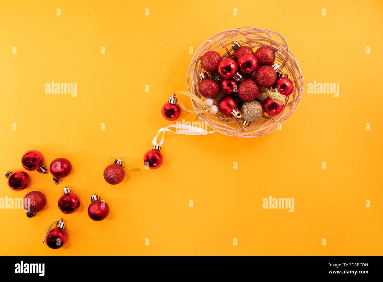 Blick von oben auf rote und goldene Weihnachtsschmuck in einem Korb. Einige Kugeln sind draußen verstreut, was verspielten Urlaubscharakter verleiht. Stockfoto