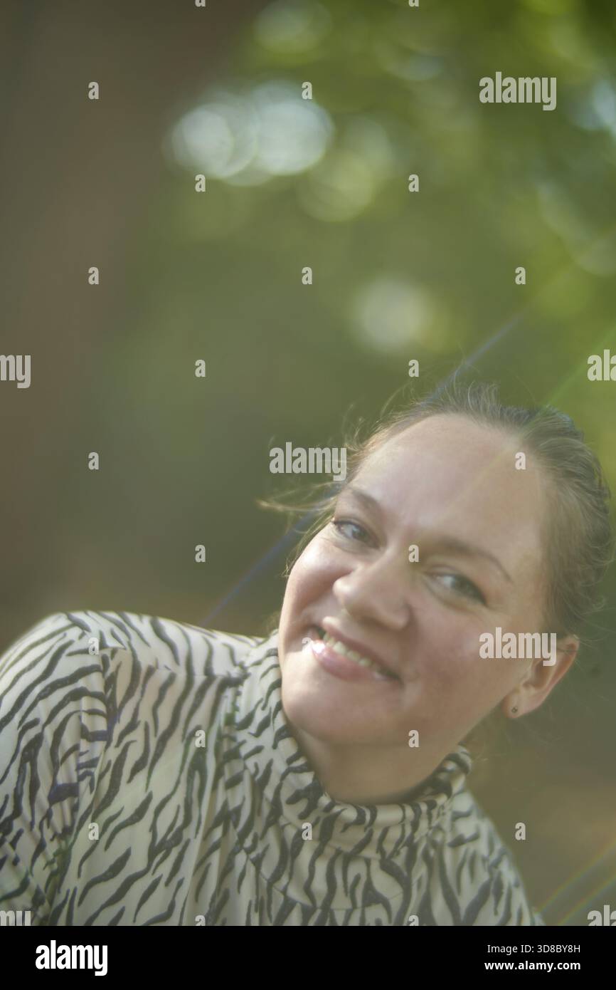 Glückliche reife ukrainische Frau in der Natur, die durch den Sonnenstrahl erleuchtet wird, gute Laune bei gutem Wetter, das Gefühl von geneigtem Glück mit innerem B Stockfoto