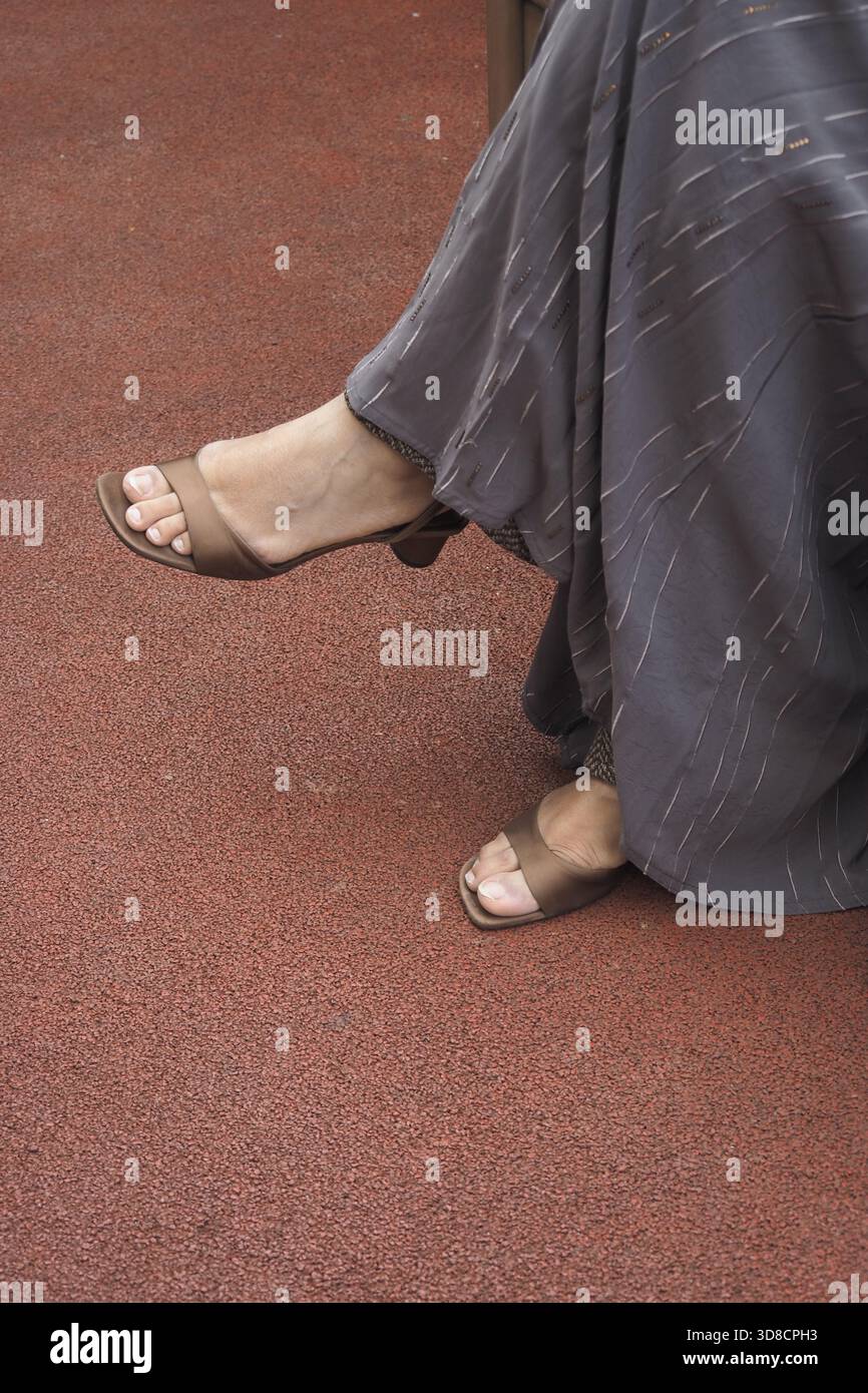 Elegante Füße in stilvollen Sandalen auf rotem Teppichboden Stockfoto