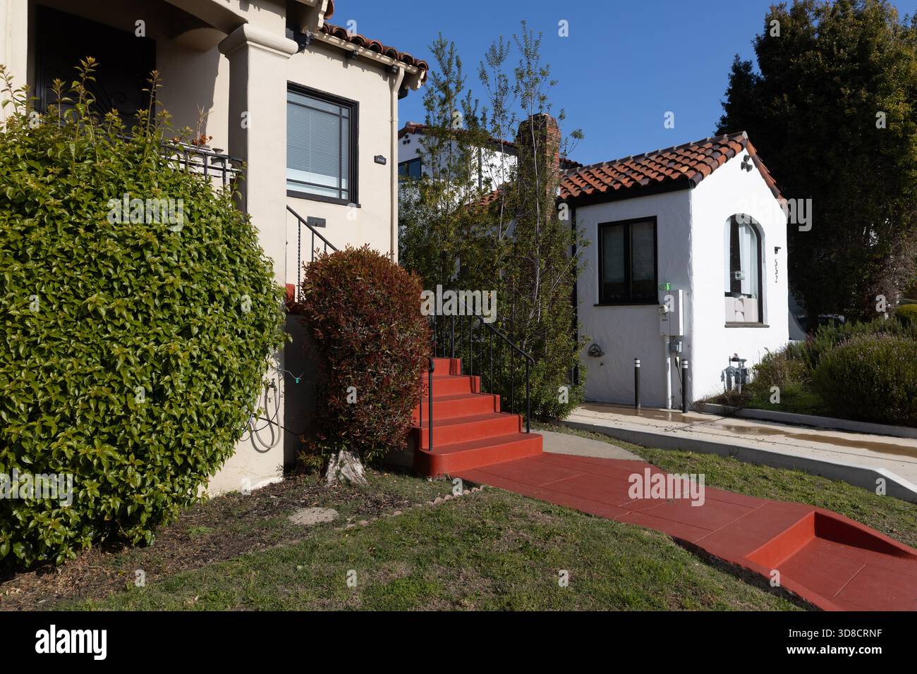 Zwei benachbarte Häuser im spanischen Stil in Oakland sind mit Stuckwänden, roten Ziegeldächern und hell bemalten Stufen ausgestattet, die von aufgeräumten Sträuchern eingerahmt werden Stockfoto