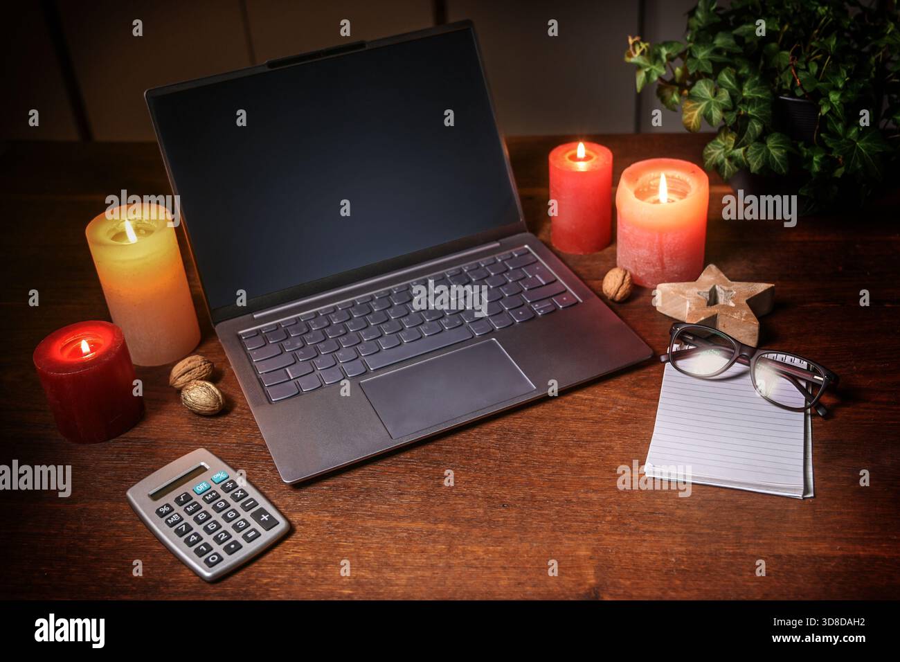 Laptop mit leerem Bildschirm, Taschenrechner und Notizblock mit Gläsern zwischen Kerzen und Weihnachtsdekoration auf einem dunkelbraunen Holzschreibtisch, Online-Shopping, Stockfoto
