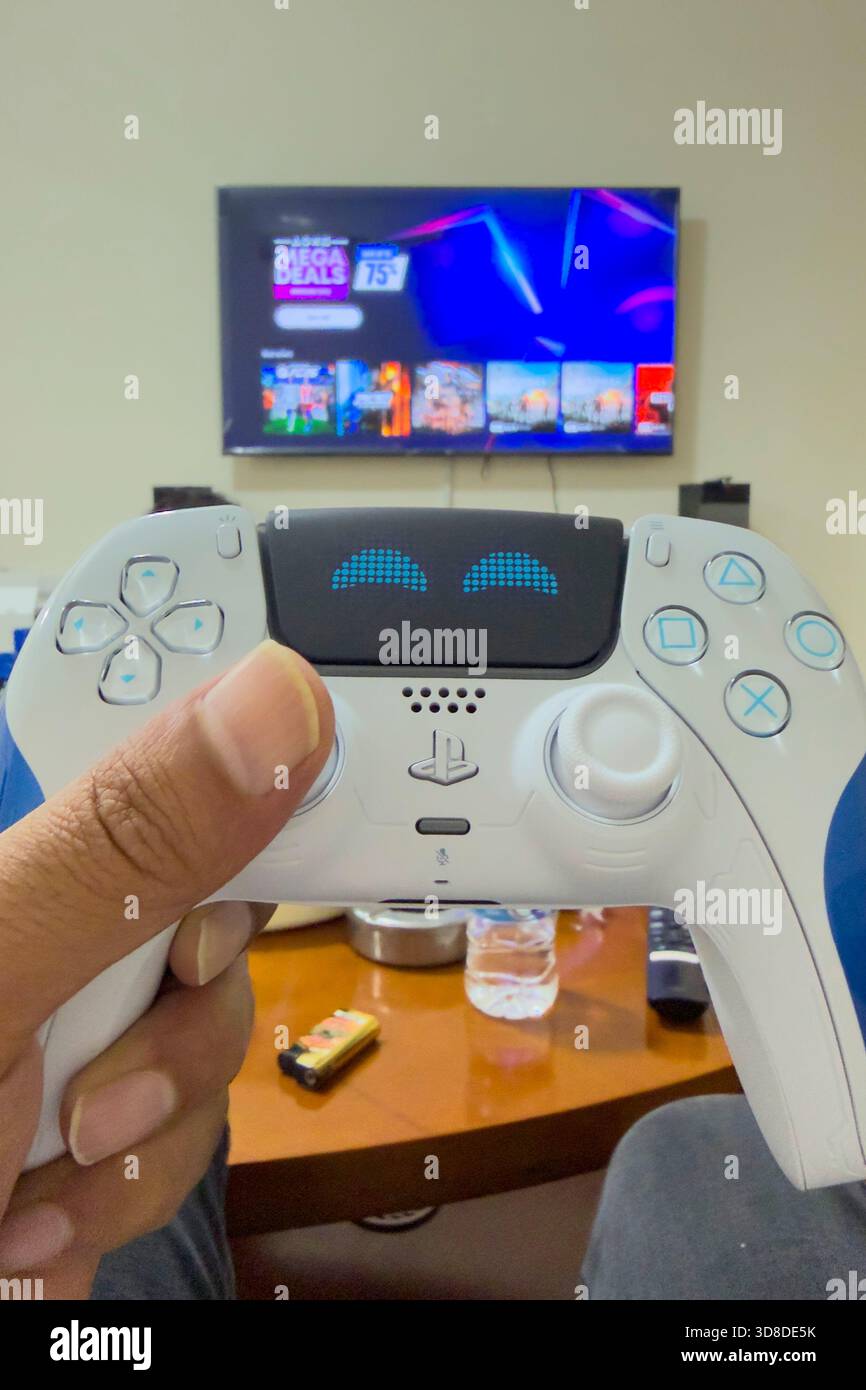 Doha, Katar - 28. November 2025: Ein Spieler spielt zu Hause Play Station 5, seine Hand hält den Dual Sense Joystick, den neuen Wireless Controller. Stockfoto