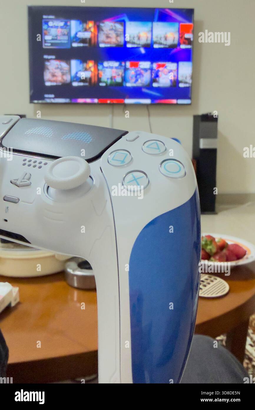 Doha, Katar - 28. November 2025: Ein Spieler spielt zu Hause Play Station 5, seine Hand hält den Dual Sense Joystick, den neuen Wireless Controller. Stockfoto
