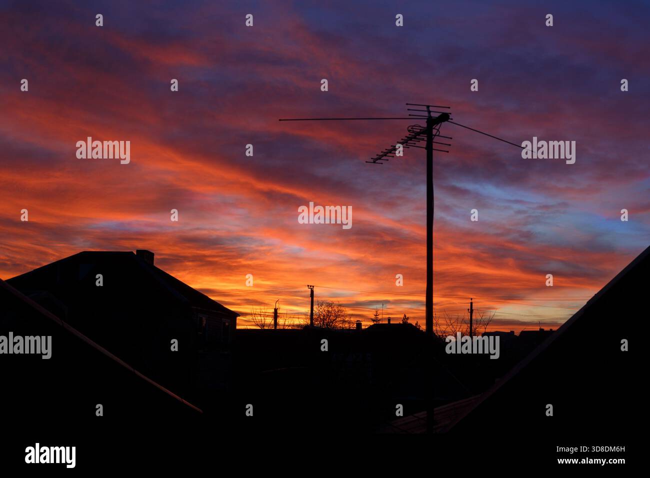 Ein heller Sonnenuntergang über den Umrissen von Häusern und eine Fernsehantenne gegen den Himmel. Stockfoto