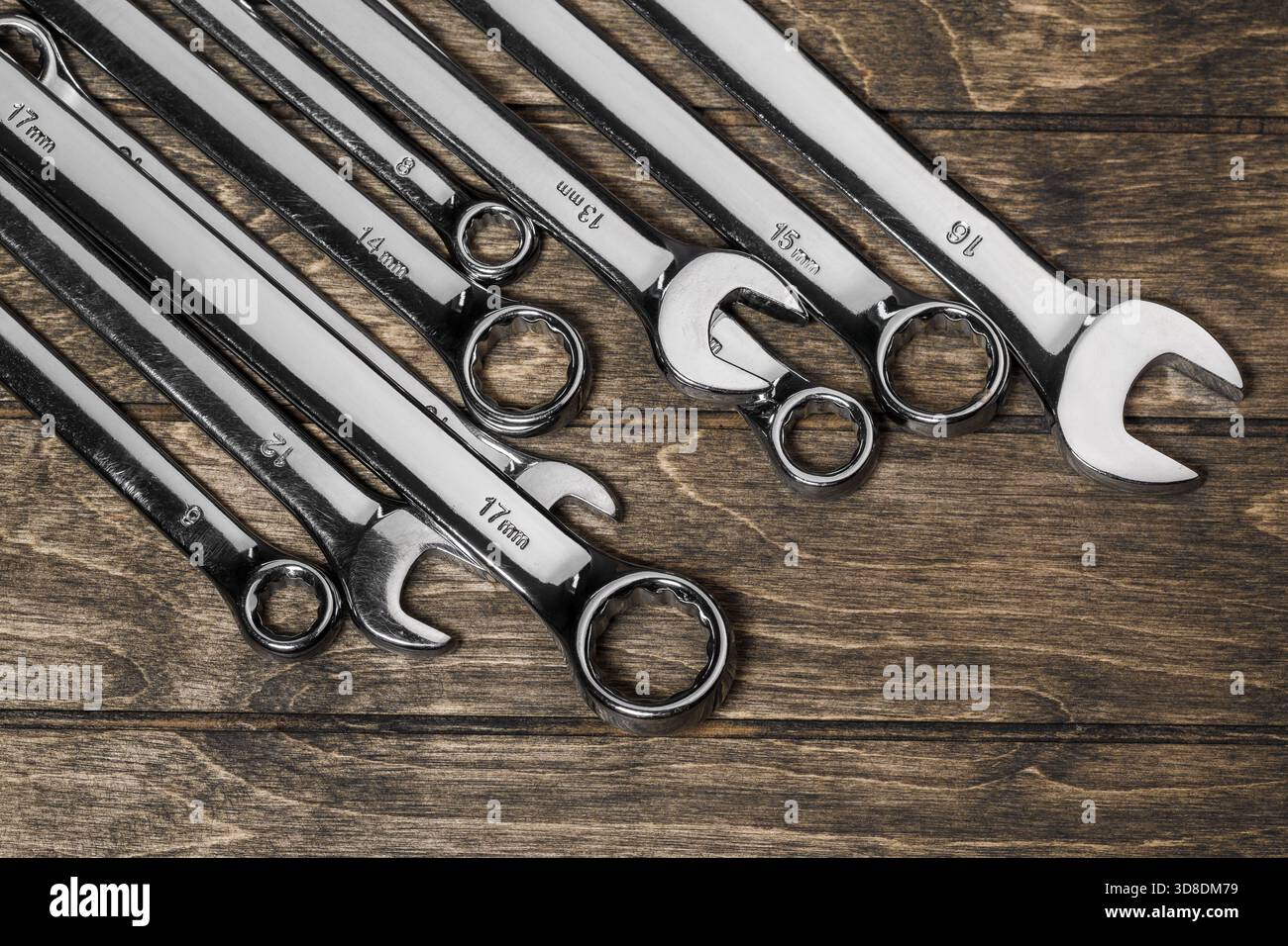 Ein Satz Maul- und Ringschlüssel in verschiedenen Größen aus Edelstahl, diagonal auf Holzuntergrund gelegt Stockfoto