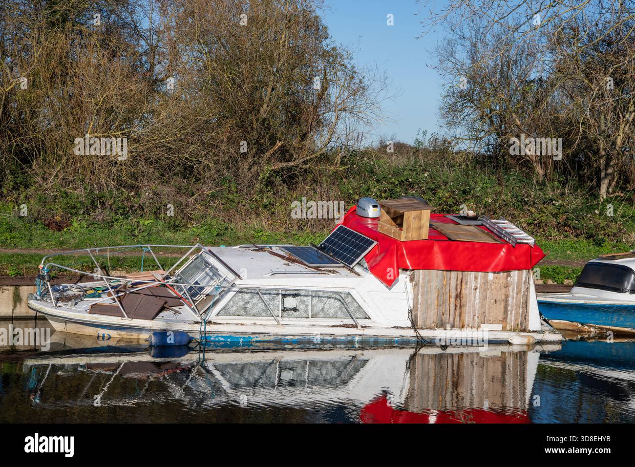 Ein Boot, das teilweise untergetaucht ist und auf dem Fluss Lea Navigation in der Nähe von Enfield Lock sinkt, gefangen in ruhigen Gewässern und natürlicher Umgebung. Stockfoto