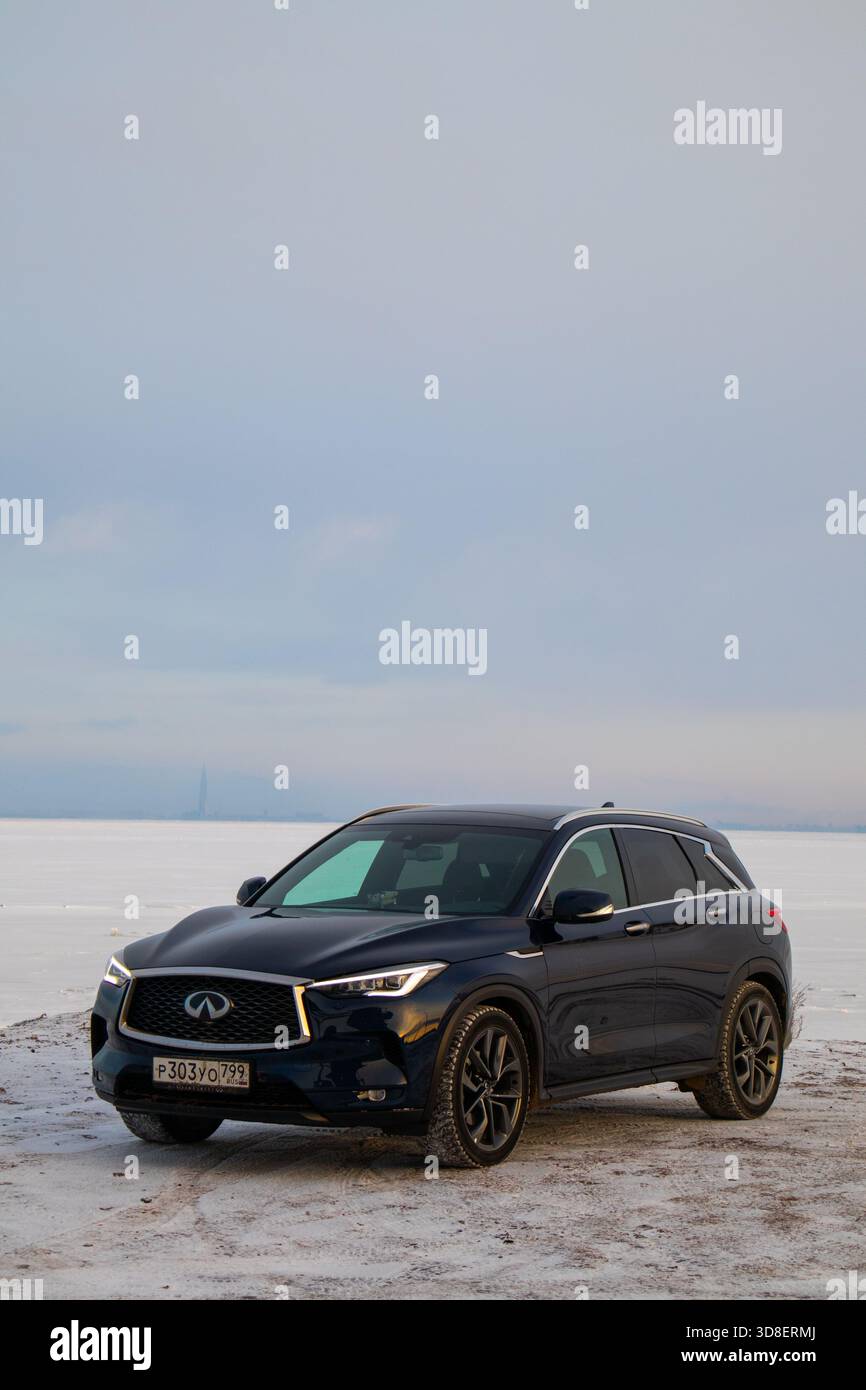 Moskau, Russland - 13. Dezember 2024: Frontansicht einer dunkelblauen Infiniti QX50-Kreuzung, die auf einer schneebedeckten Ebene mit einem riesigen fla geparkt ist Stockfoto