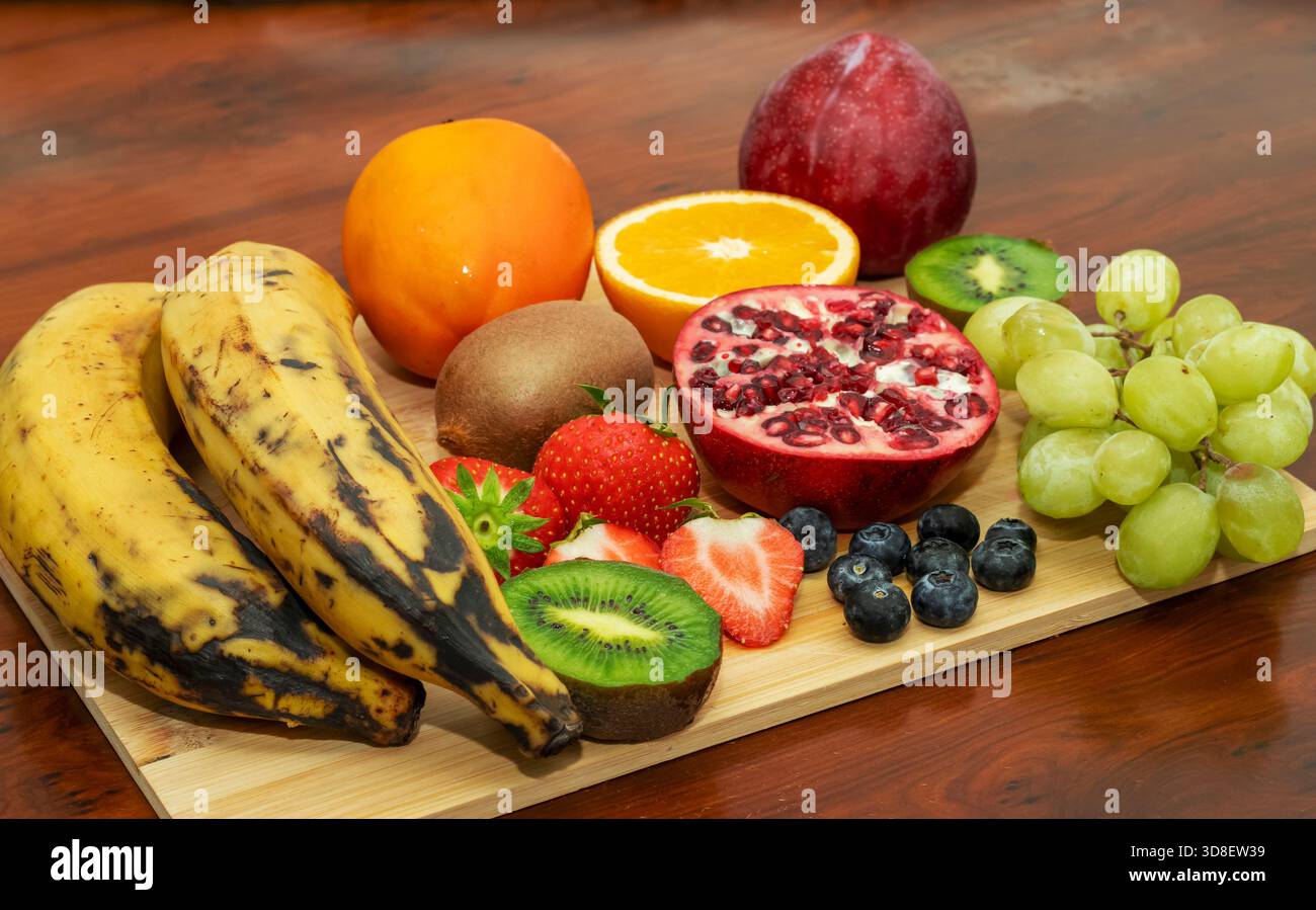 Bunte frische Obstplatte mit Kochbananen, Granatapfel, Kiwi, Beeren, Orange, Trauben, für gesunde Ernährung Stockfoto