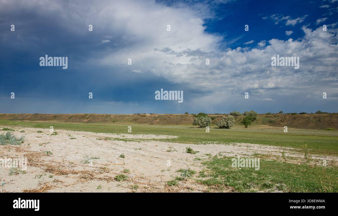 Weite Steppenlandschaft in der Region Cherson, Ukraine mit einem niedrigen horizontalen Uferdamm am Horizont, einem grünen Grasstreifen und einer sandigen Deckdecke im Vordergrund Stockfoto