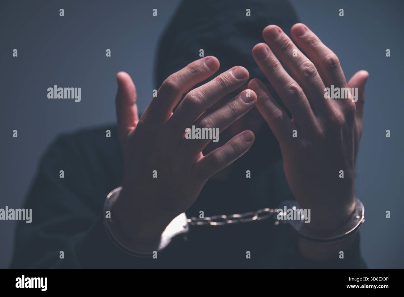 Düsteres, stimmungsvolles Bild eines vermummten Täters, der sein Gesicht hinter gefesselten Händen versteckt, aufgenommen bei schlechten Lichtverhältnissen, um Verbrechen, Angst und emotionale Not zu vermitteln. Auswahl Stockfoto