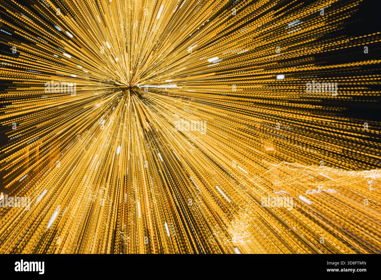 Abstraktes Bild mit Bewegungsunschärfe von goldenen Weihnachtslichtern, die nach außen Streifen und einen energetischen Starburst-Effekt erzeugen Stockfoto