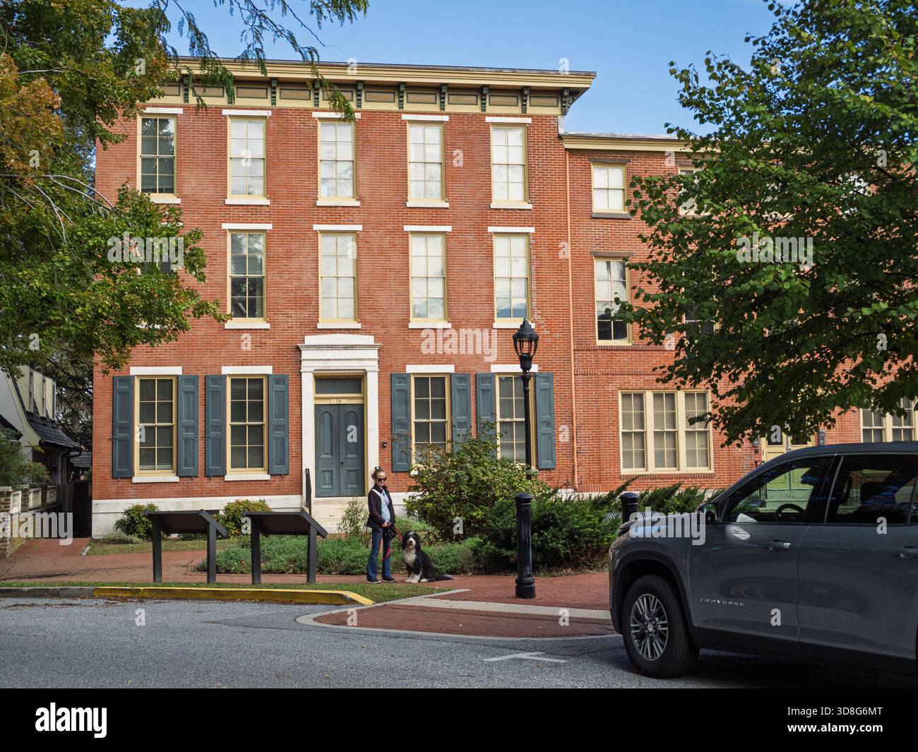 Die rote Backsteinfassade des Early Choice Gebäudes in Dover, Delaware, mit einer Person und einem Border Collie auf dem Bürgersteig. Stockfoto