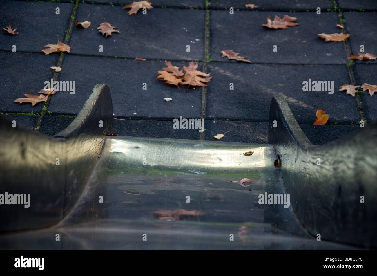 Herbstlaub auf leerem Spielplatz Rutsche und Gummiboden Stockfoto