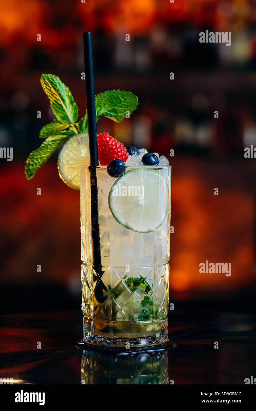 Limettencocktail mit Minze-Limette, Crushed Ice, Erdbeere, Heidelbeere und frischer Beilage in einem gemusterten Glas. Stockfoto