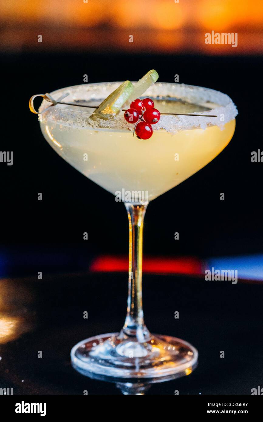 Ein hellgelbes Getränk in einem Margarita-Glas mit gesalzenem Rand, Limettenkeilen und roten Beeren gegen ein warmes Stockfoto
