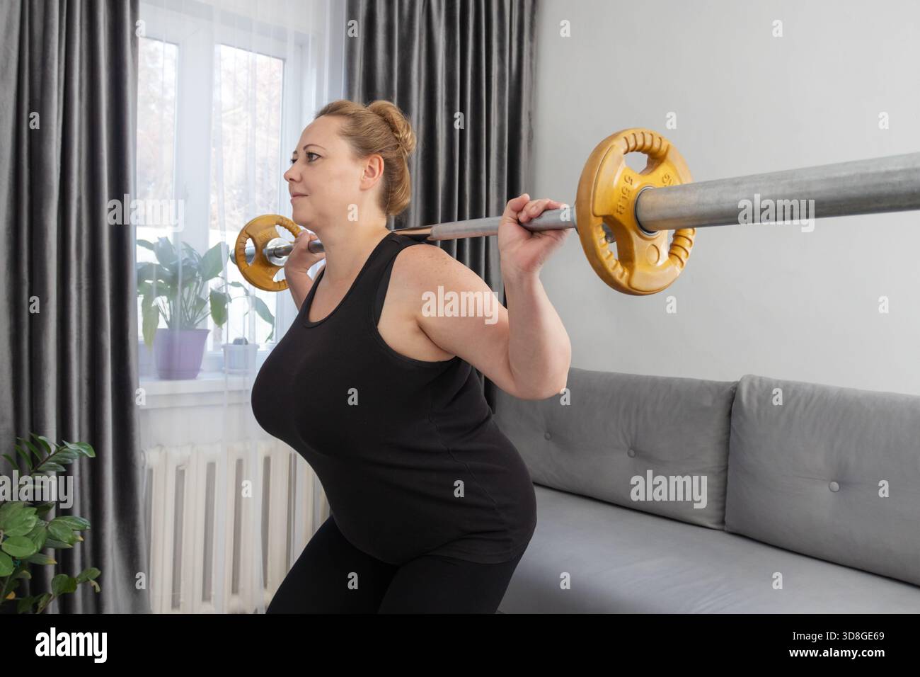 Eine Frau mittleren Alters macht Langhantelhocken zu Hause. Konzepte Fitness Reise, Körper positive Gesundheit, Home Gym Workout, Krafttraining. Stockfoto