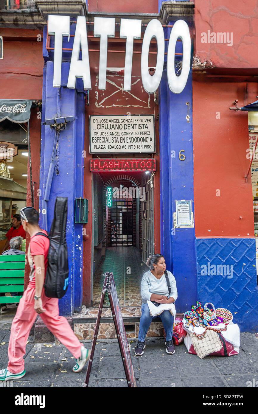 Mexiko-Stadt Mexiko, Coyoacan, Tattoo Salon Zahnarzt Schild, Straßenverkäufer Frau Erwachsene Hispanic sitzt neben der Tür und verkauft handgemachte Handarbeit gestickt t t Stockfoto