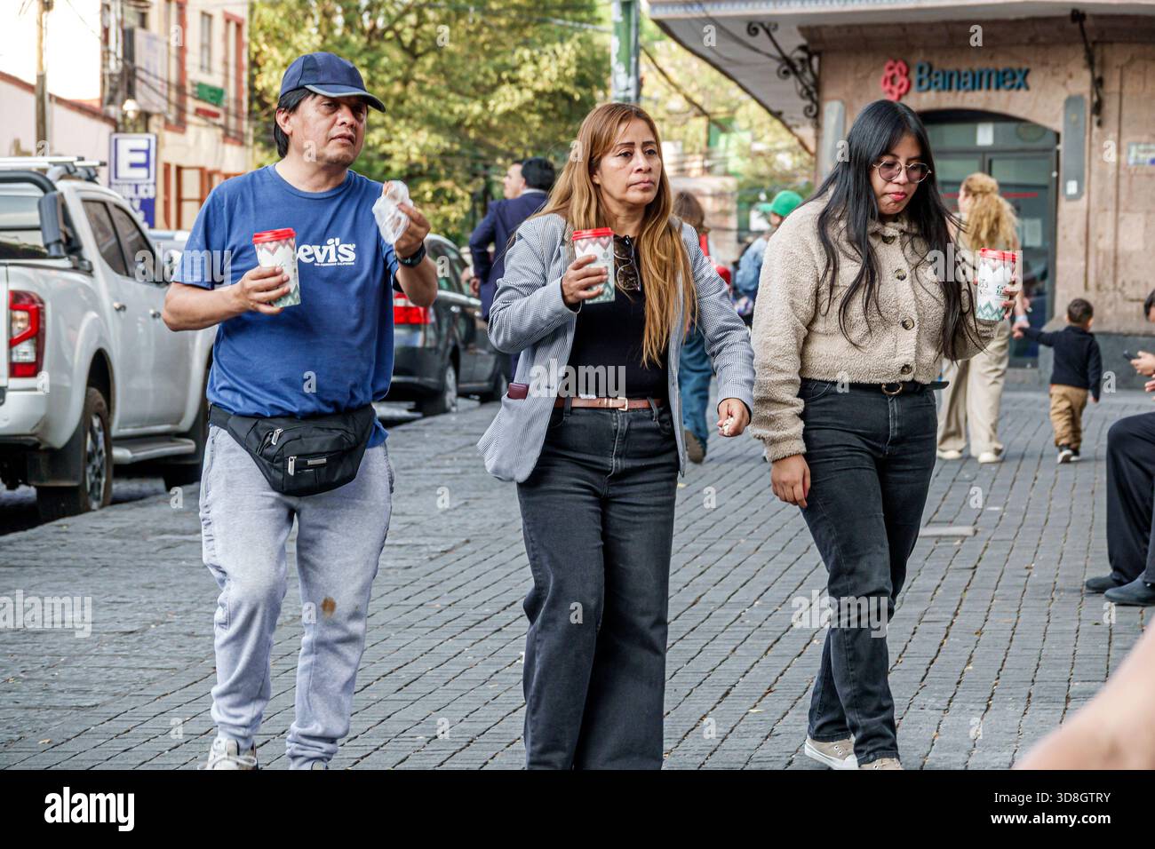 Mexiko-Stadt Mexiko, Coyoacan, hispanisch erwachsener Mann Frauen Fußgänger mit Kaffeetassen lässige Kleidung konzentrierte Ausdrücke bewegen sich entlang Kopfsteinpflaster Stockfoto